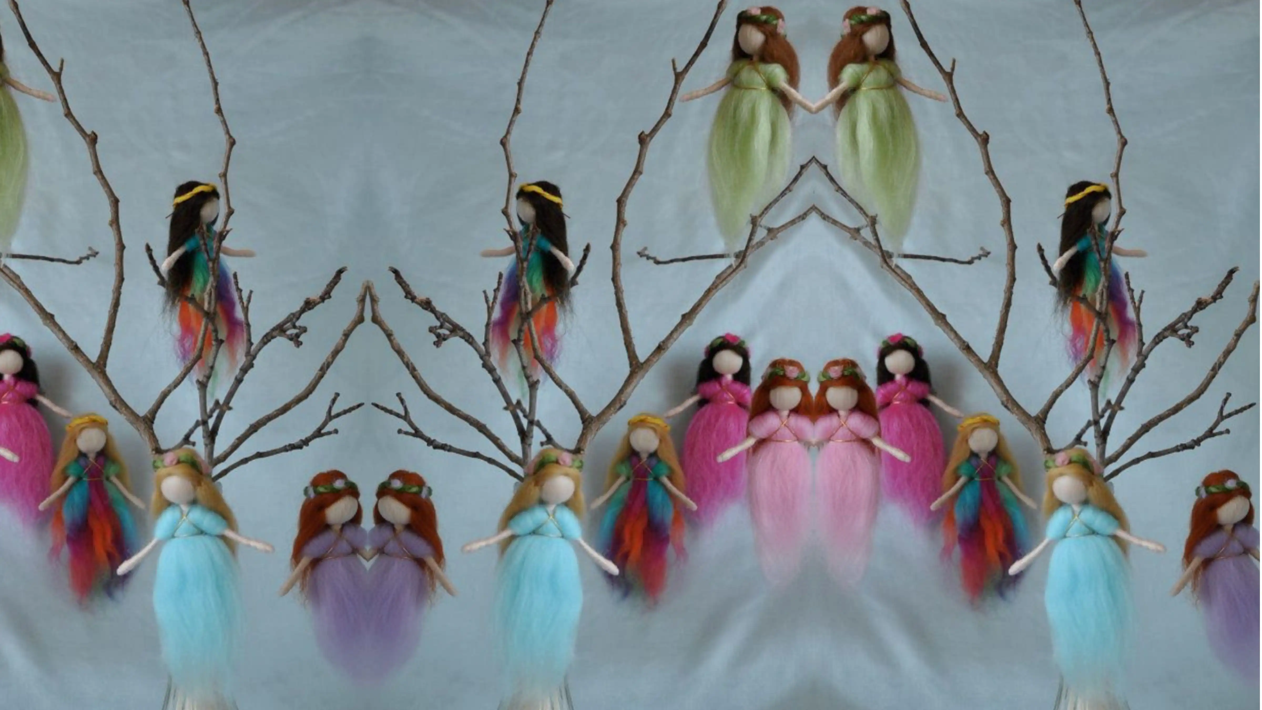 CoColourful handmade fairy dolls hang from branches in a mirrored display on a soft blue background.